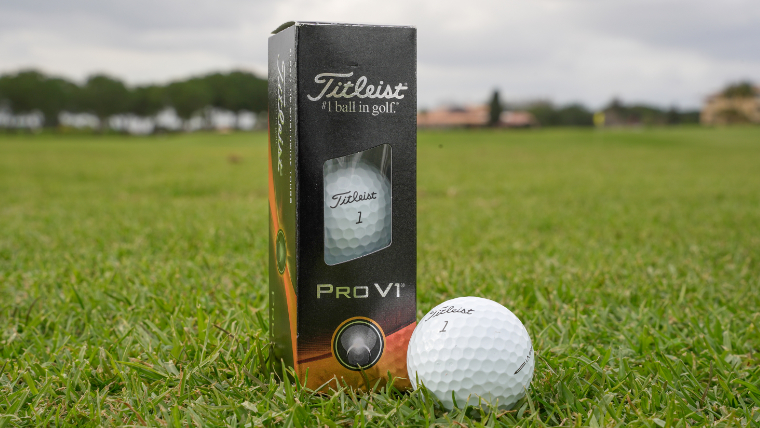 a-sleeve-of-titleist-prov1-golf-balls-next-to-a-single-golf-ball-resting-on-grass