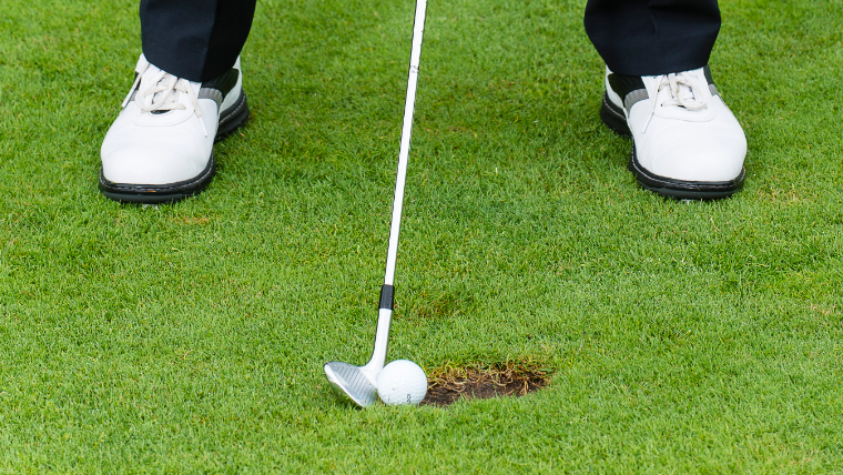 a-close-up-of-a-golfer-addressing-his-ball-that's-on-the-edge-of-a-divot