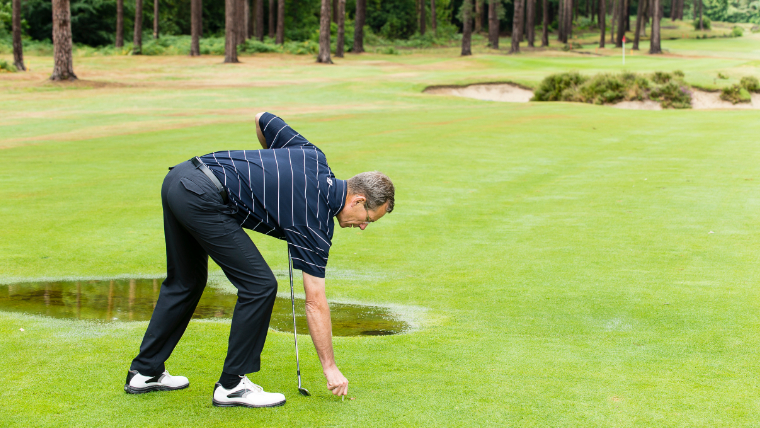 a-golfer-placing-his-ball-on-the-fairway-near-a-stretch-of-standing-water