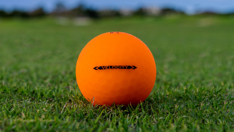 an-orange-titleist-velocity-golf-ball-resting-on-grass
