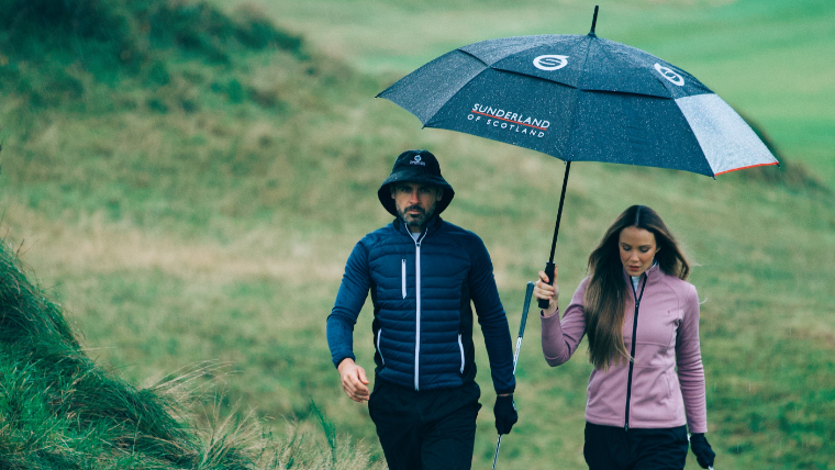 two-golfers-walking-down-a-fairway-under-an-umbrella