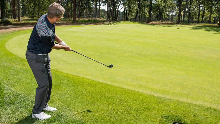 a-golfer-hitting-a-hybrid-beside-a-green