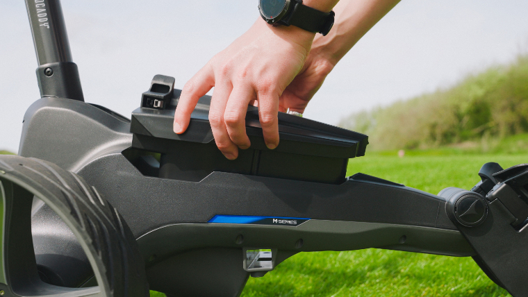 a-golfer-putting-a-battery-in-a-motocaddy-electric-trolley