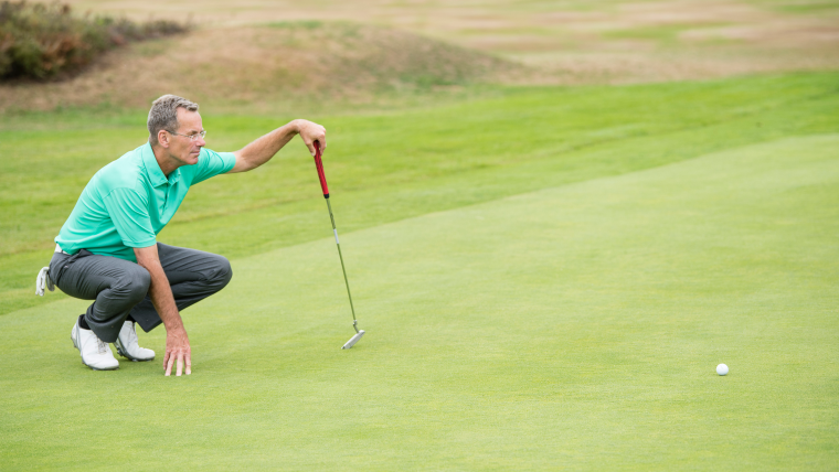 a-golfer-kneeling-next-to-his-ball-on-the-green