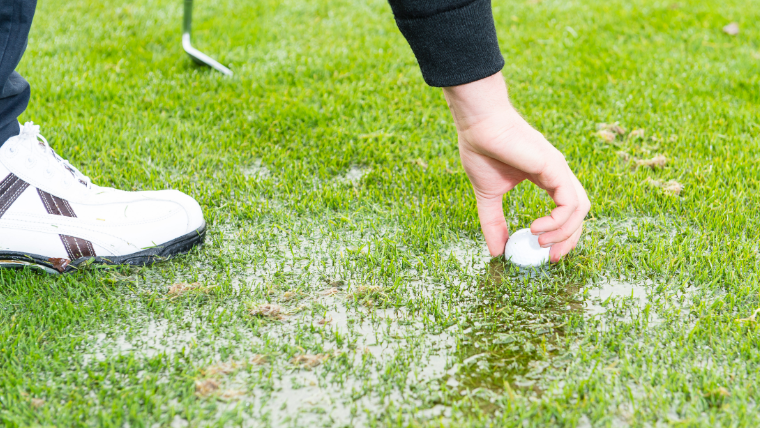 a-golfer-reaching-for-a-ball-on-a-wet-fairway