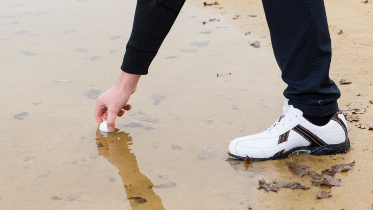 a-golfer-reaching-for-a-ball-in-a-wet-bunker